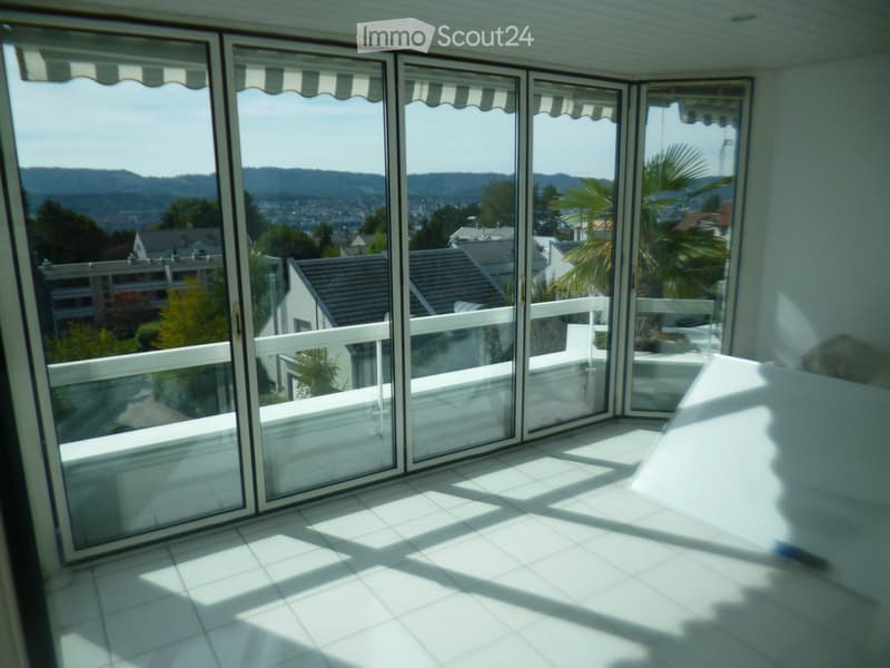 Bright, tiled balcony with large sliding glass doors offering a scenic view of the city and surrounding hills.