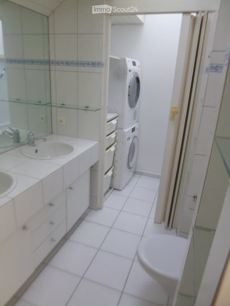 Bathroom with white tiled floor, sink with mirror, washing machine, and toilet.