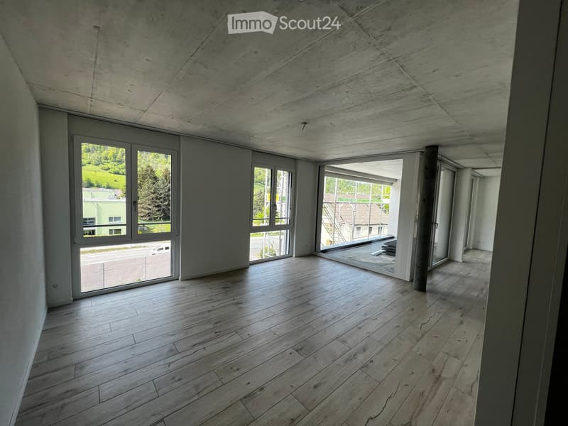 Empty room with wooden flooring, large windows, and a concrete ceiling. No furniture or equipment present.