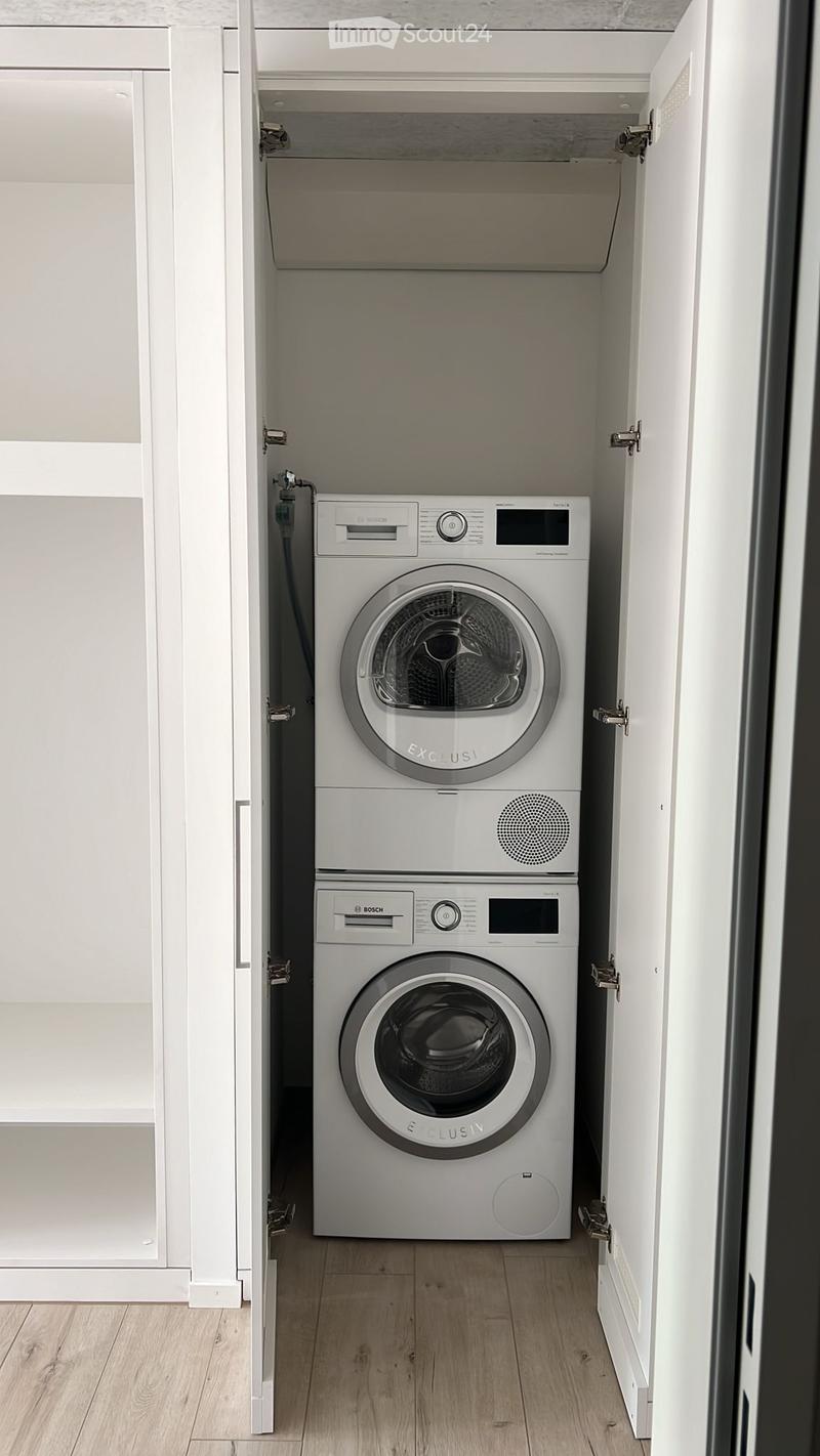 Compact bathroom with a stacked washing machine and dishwasher unit, white cabinetry, and wooden flooring.