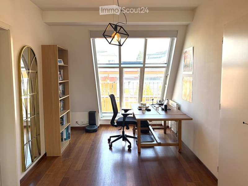 Modern, well-lit room with wooden flooring, large window, desk, ergonomic chair, bookshelf, and decorative mirror.