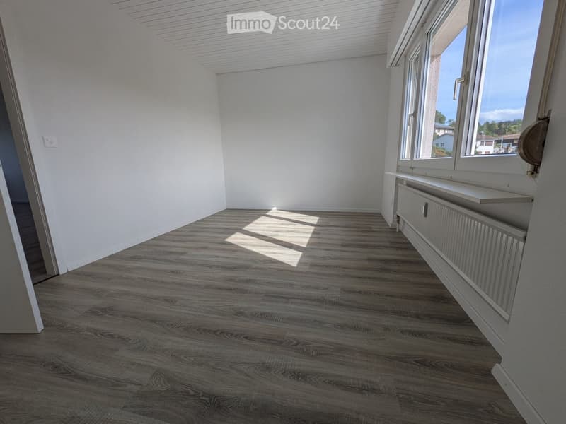 Empty room with wooden flooring, white walls, large windows, and a radiator under the windows.
