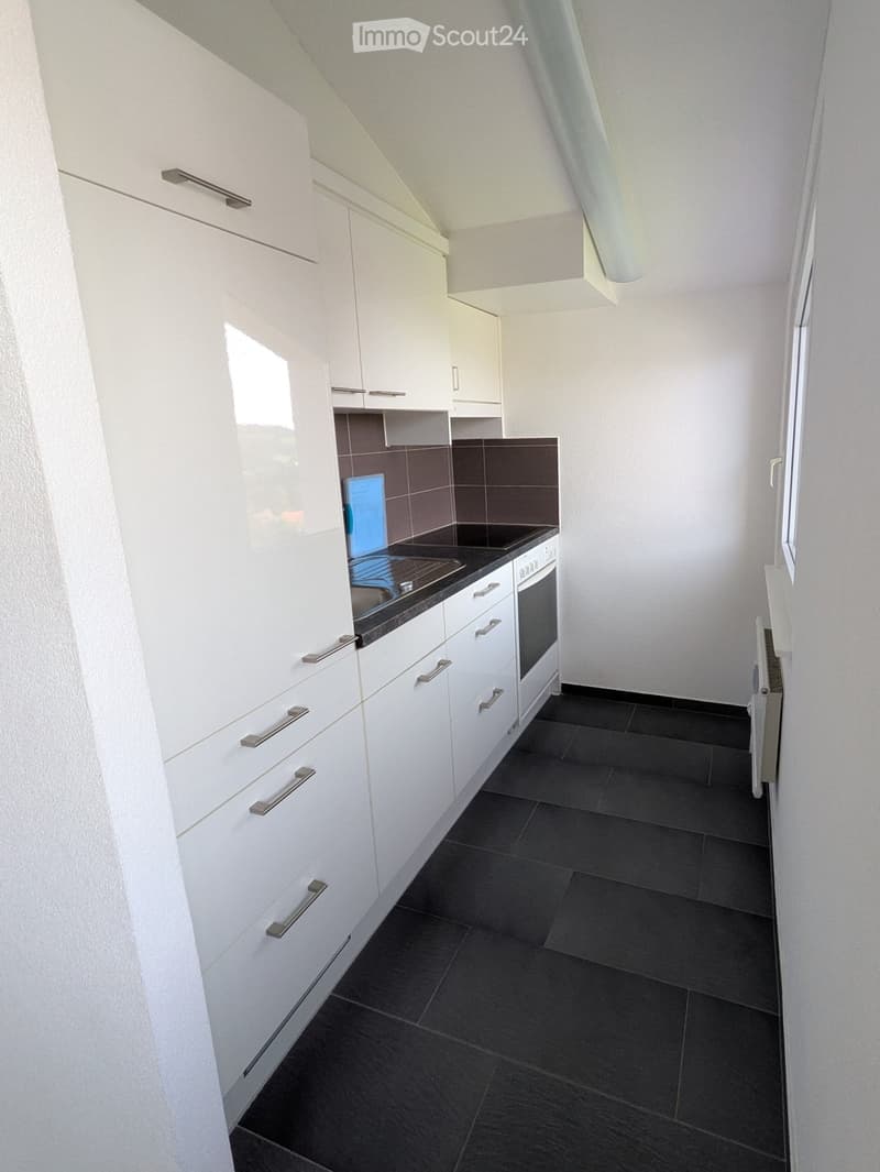 Modern kitchen with white cabinets, dark countertops, and a built-in oven. The space features sleek metallic handles and a dark tiled floor.
