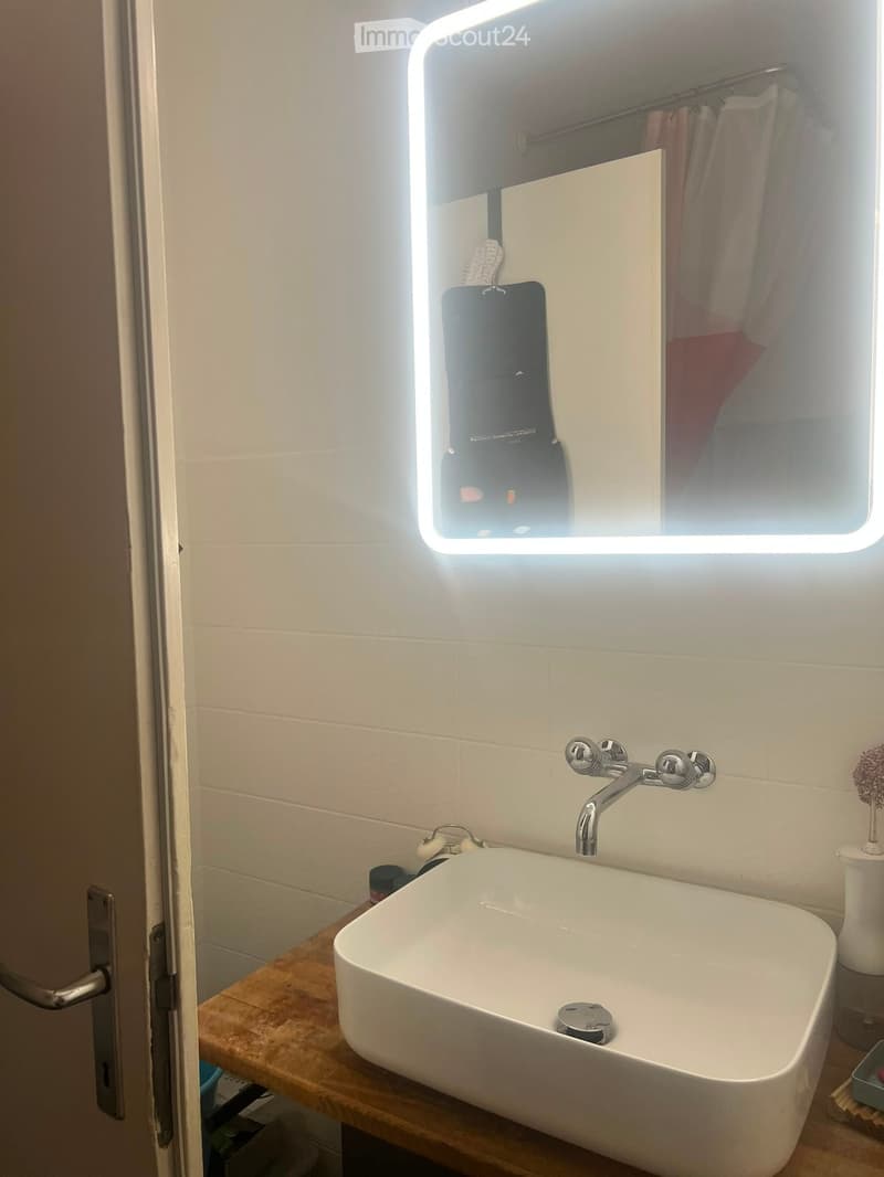 Modern bathroom with a white sink, chrome faucet, illuminated mirror, and a small decorative vase on the counter.