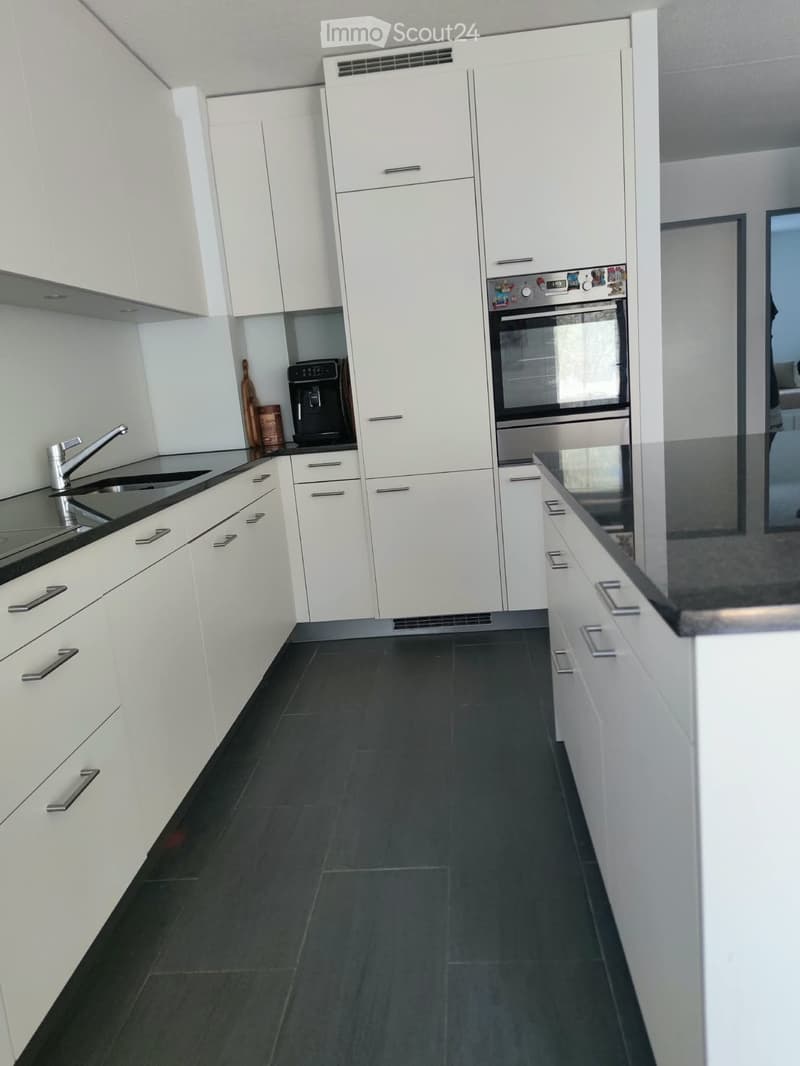 Modern kitchen with white cabinets, dark tiled floor, stainless steel sink, faucet, oven, and coffee machine.