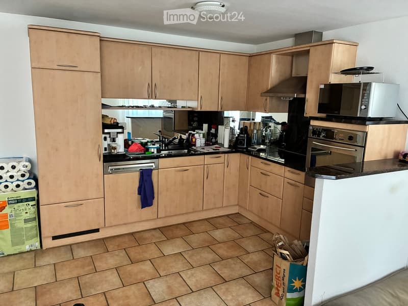 Well-equipped kitchen with light wooden cabinets, stainless steel appliances, and a tiled floor.