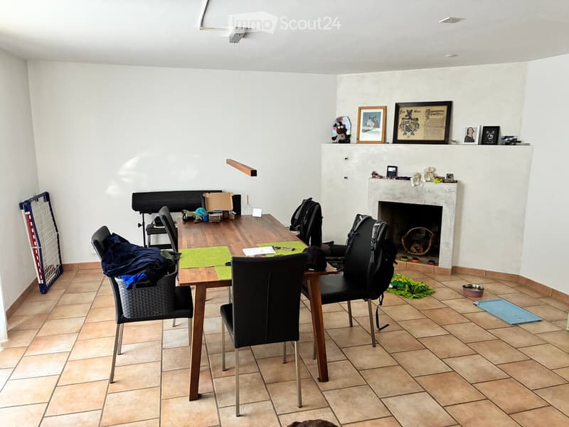 Living room with tiled floor, fireplace, table, chairs, and various items including backpacks and a wicker basket.