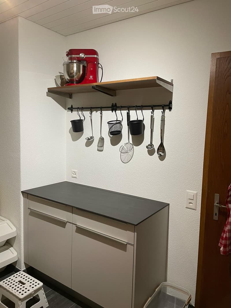 Modern kitchen with a black countertop, white cabinets, a mixer on a shelf, and hanging pots and pans.