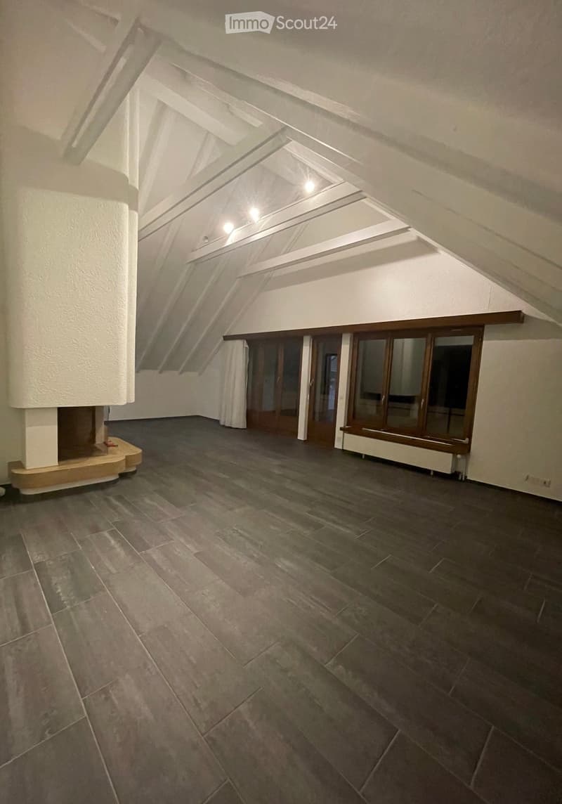 Empty attic space with exposed wooden beams, skylights, and dark tiled flooring. No furniture or equipment visible.