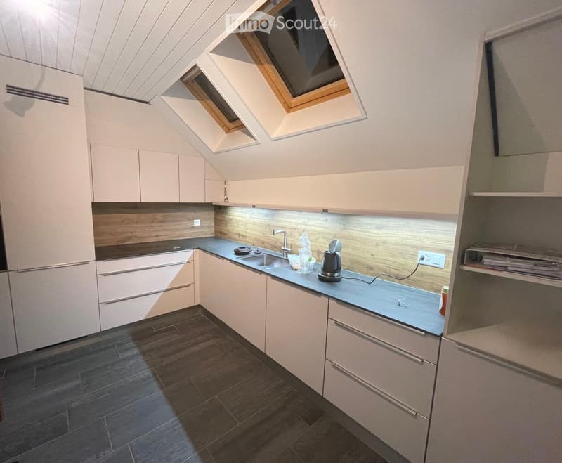 Modern kitchen with light-colored cabinets, dark countertops, and a dark tiled floor. Features include a sink, faucet, and small appliances on the counter.
