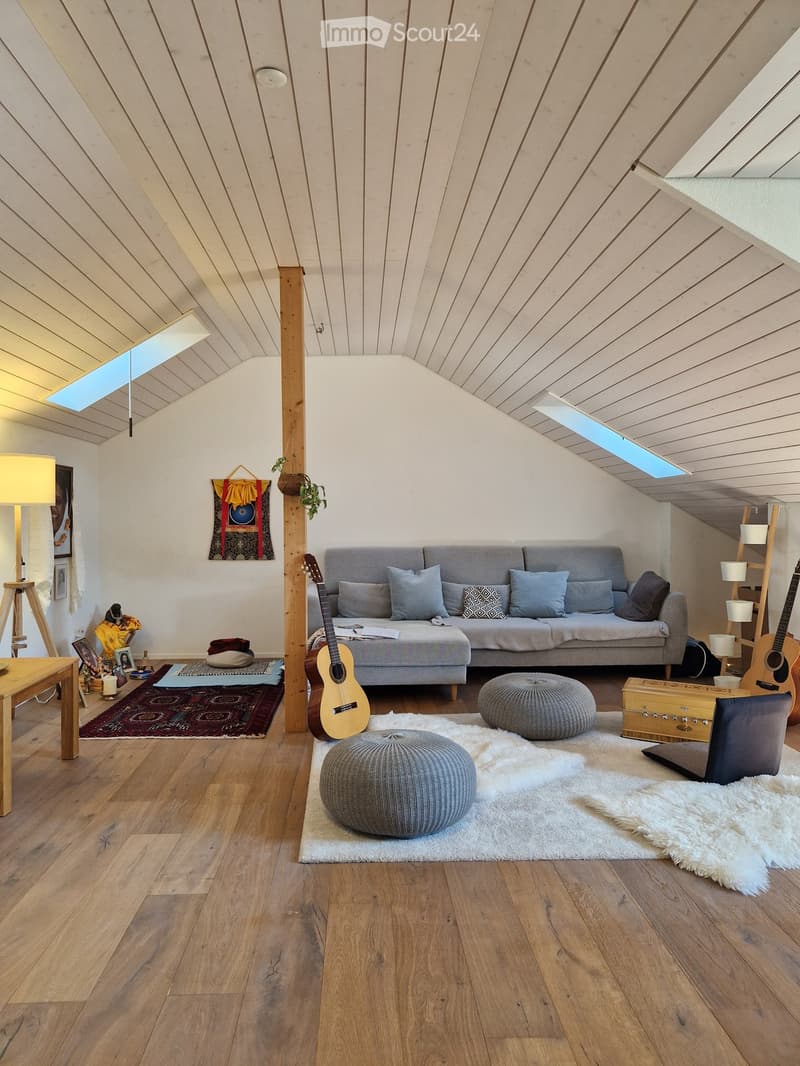 Living room with wooden floors, grey sofa, two round stools, guitar, small table, and decorative items.