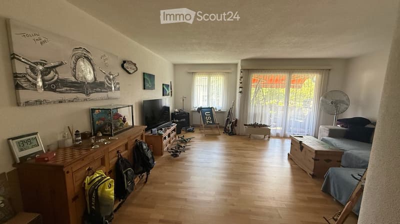 Living room with wooden flooring, large windows, sofa, fish tank, guitar, fan, and various decorative items.