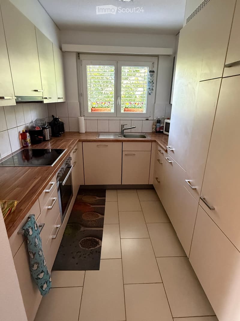 Modern kitchen with light-colored cabinets, wooden countertops, and tiled floor. Features an oven, sink, microwave, and various kitchen appliances.