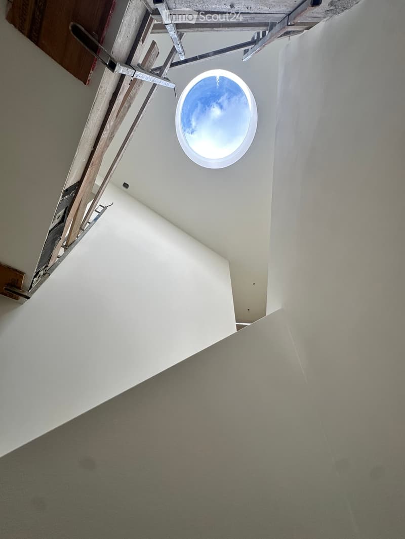 Empty hallway with white walls, carpeted floor, and a circular skylight showing a blue sky.