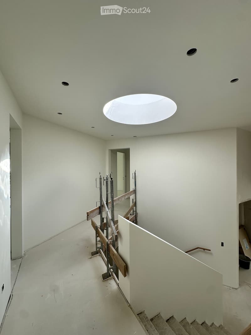 Empty hallway with white walls, a skylight ceiling, and a staircase under construction with wooden railings and metal supports.