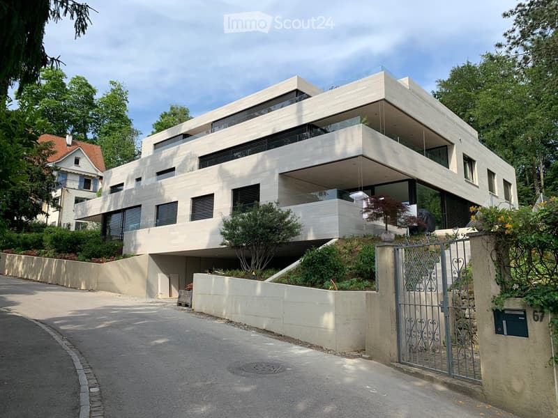 Modern design house, white exterior, glass balcony, gated entrance, surrounded by greenery