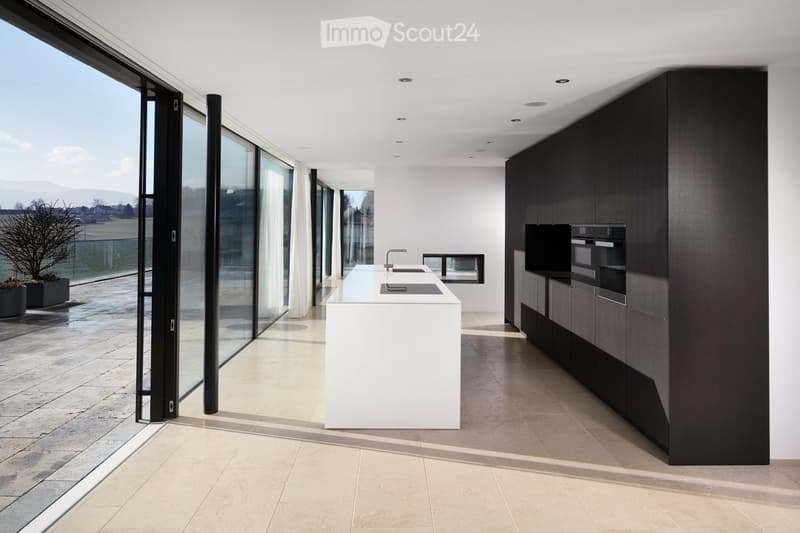 modern kitchen with large white central island, black cabinets, open space with large windows leading to terrace, ovens and sink in corner, minimalist design