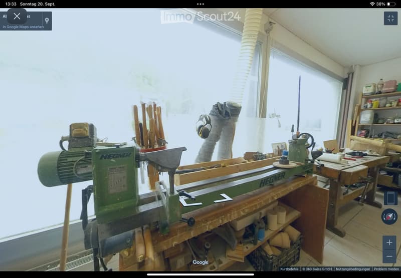 Well-lit workshop with a lathe machine, workbench, shelves filled with tools, and various wooden materials.