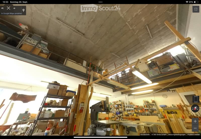 A spacious workshop with exposed concrete ceiling, various tools, workbenches, shelves filled with supplies, and wooden materials.