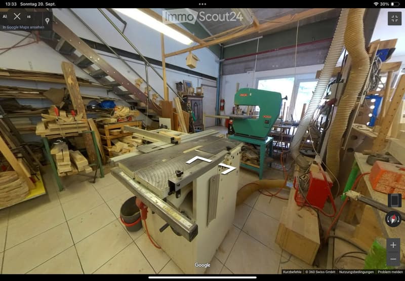 Workshop with various woodworking tools, including a table saw, band saw, and workbench, surrounded by stacks of wood and materials.