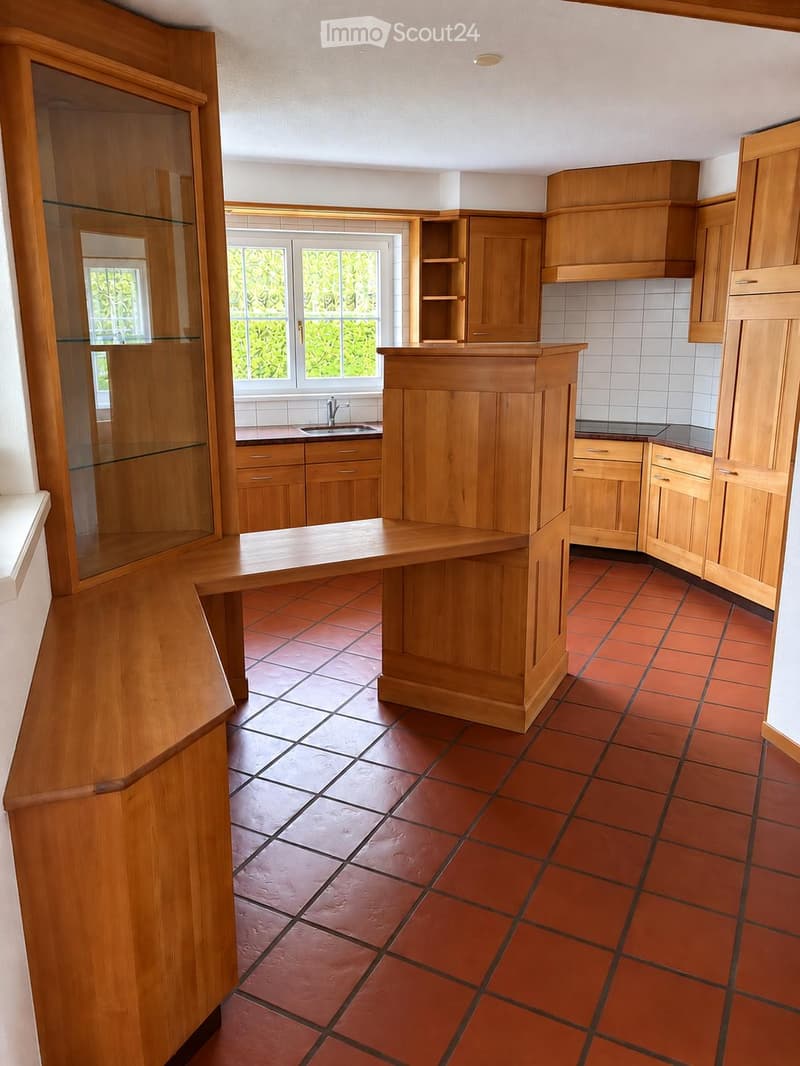 Bright kitchen with wooden cabinets, a central island, and red tiled flooring.