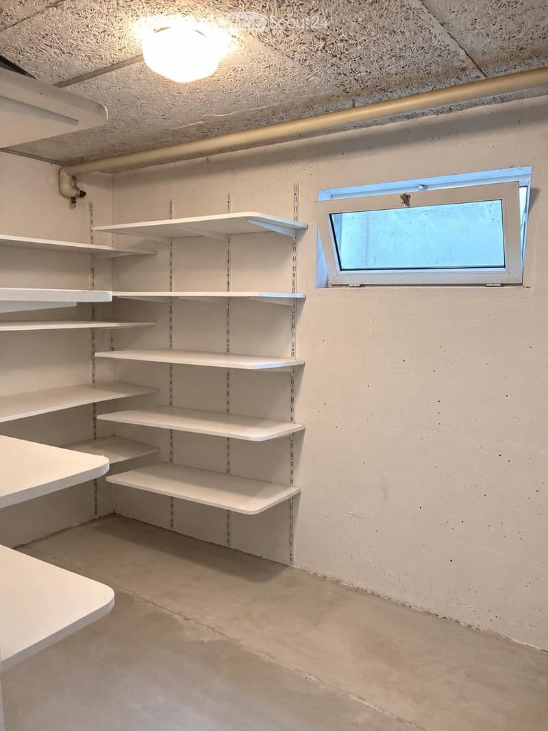 Empty storage room with white shelves, a small window, and a round ceiling light fixture.