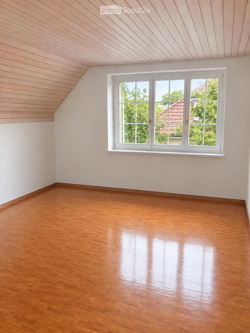 Empty room with wooden flooring and white walls, featuring a large window with white frame and multiple panes, allowing natural light to enter.