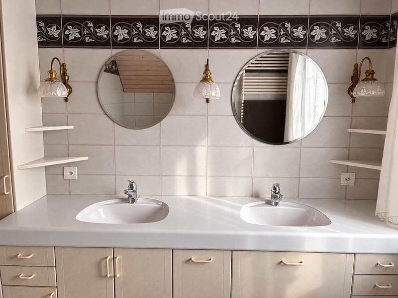 Bathroom with double sink, two round mirrors, decorative wall tiles, and light fixtures.