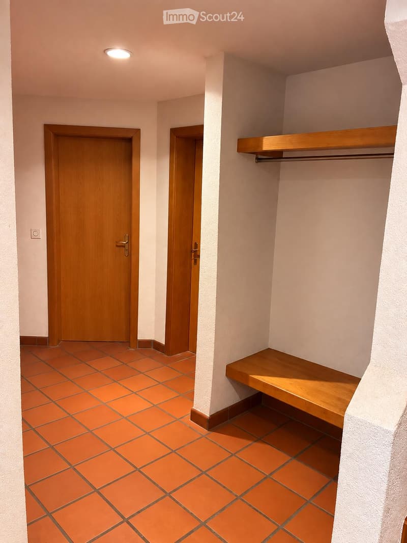 Empty hallway with orange tiled floor, white walls, two wooden doors, and a wooden bench with a shelf.