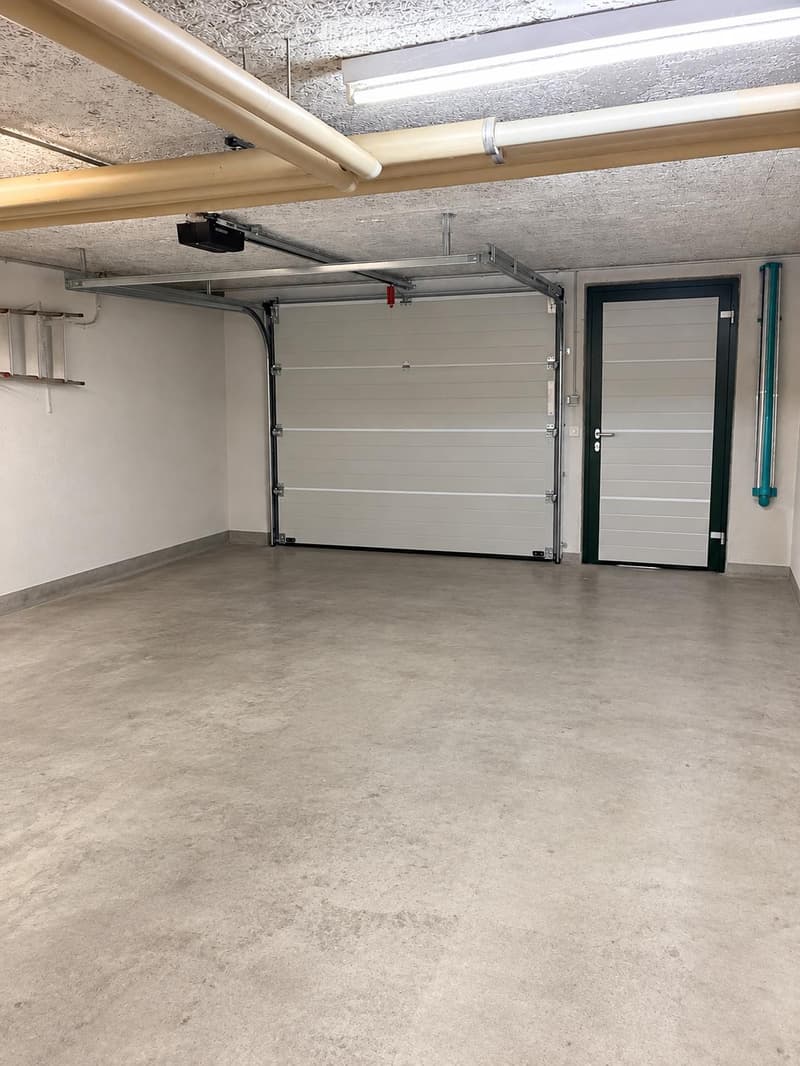 Empty garage with concrete floor, white walls, and a large overhead door.