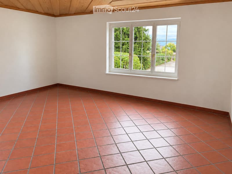 Empty room with red tiled floor and white walls, featuring a large window with white frame showing greenery outside.