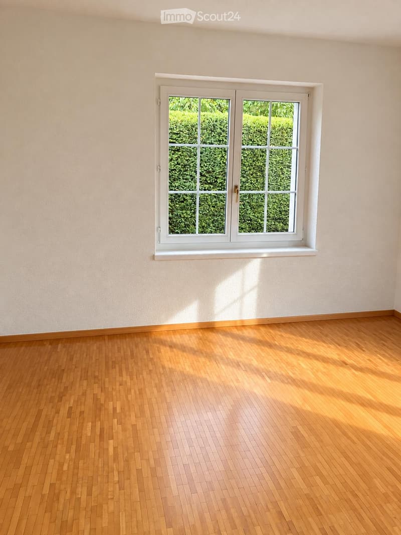 Empty room with wooden flooring and a large window showing greenery outside. No furniture or equipment present.