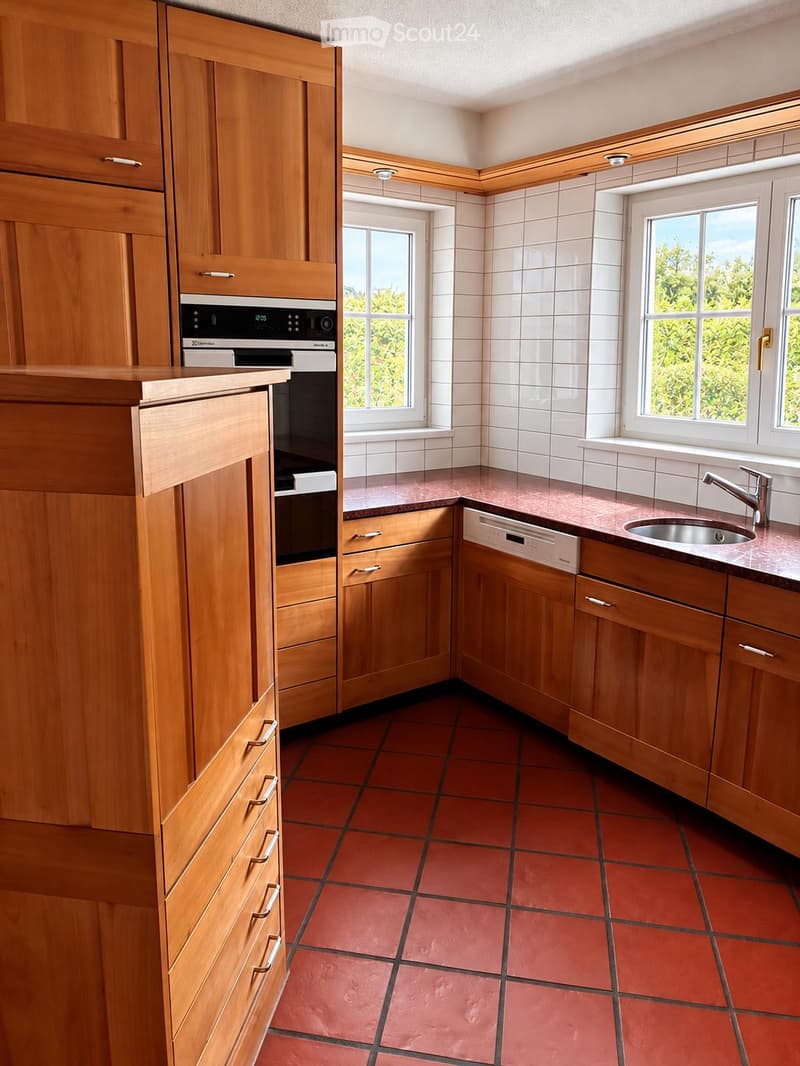 Modern kitchen with wooden cabinets, red tiled floor, and stainless steel appliances including an oven and dishwasher.