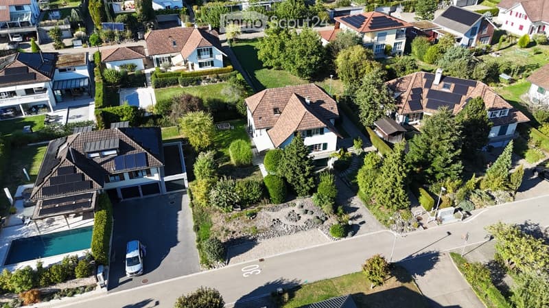 Aerial view of a residential neighborhood with multiple houses, solar panels, a swimming pool, and a driveway with a parked car.