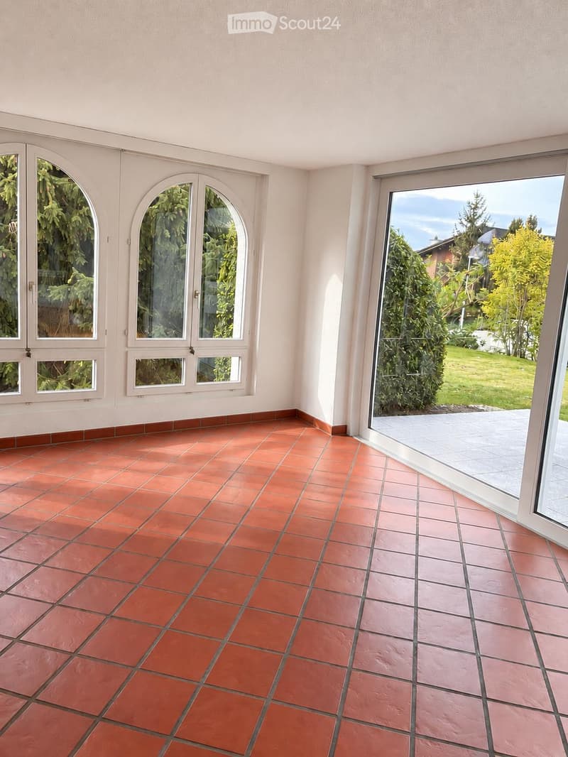 Empty room with terracotta tiled floor, white walls, large windows, and sliding glass door leading to outdoor area.