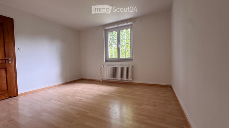 Empty room with light pink walls, wooden floor, a window with white frame, and a radiator below it.