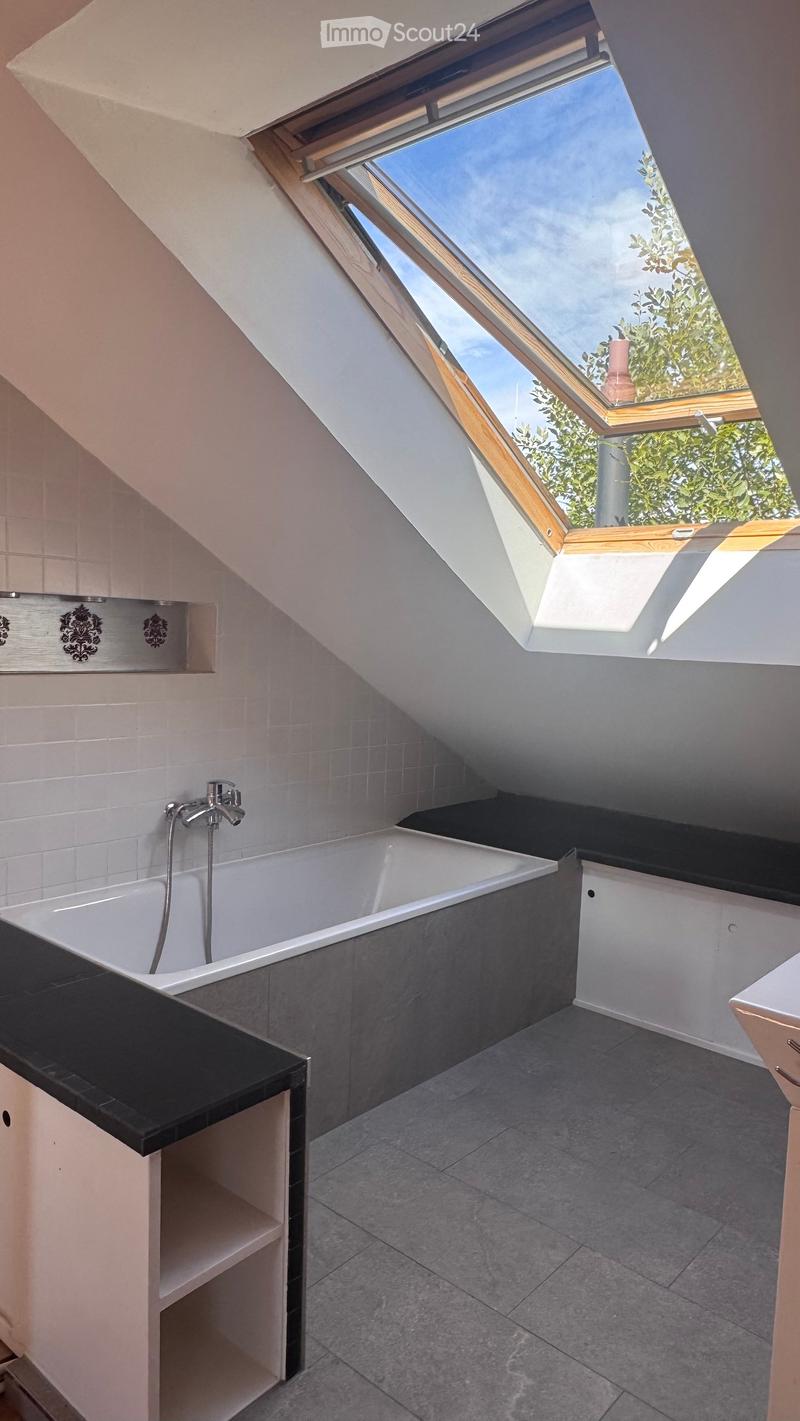 Modern bathroom with a large skylight window, white tiled walls, grey tiled floor, bathtub, and built-in cabinetry.
