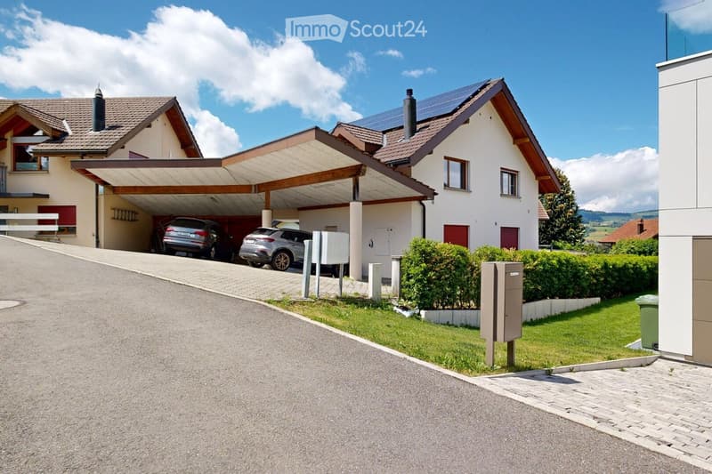 Two-story house with a covered driveway, two parked cars, solar panels on the roof, and a well-maintained garden with hedges.