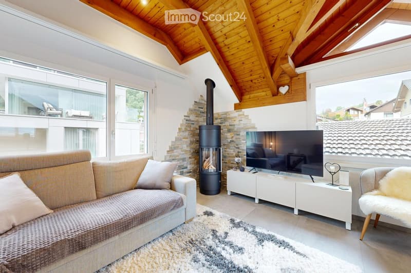 Modern living room with a wooden slanted ceiling, large windows, a fireplace, a sofa, a coffee table, a television, and a decorative chair.