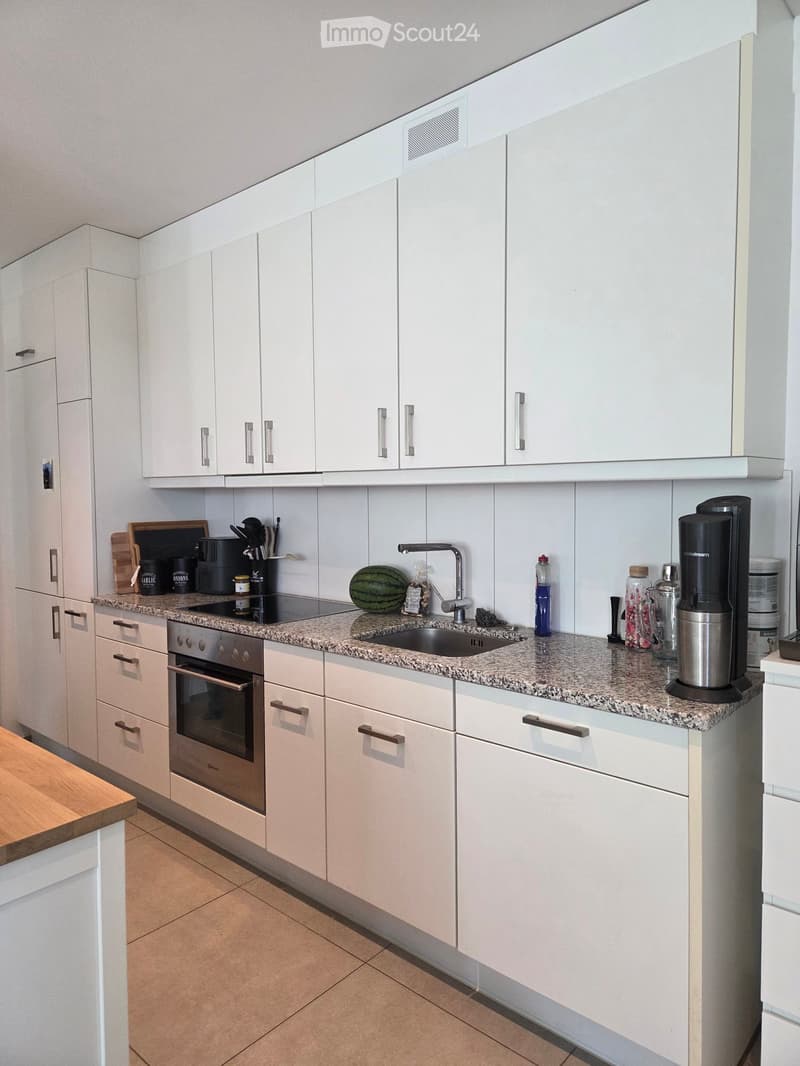 Modern kitchen with white cabinets, granite countertop, built-in oven, sink, and various appliances.