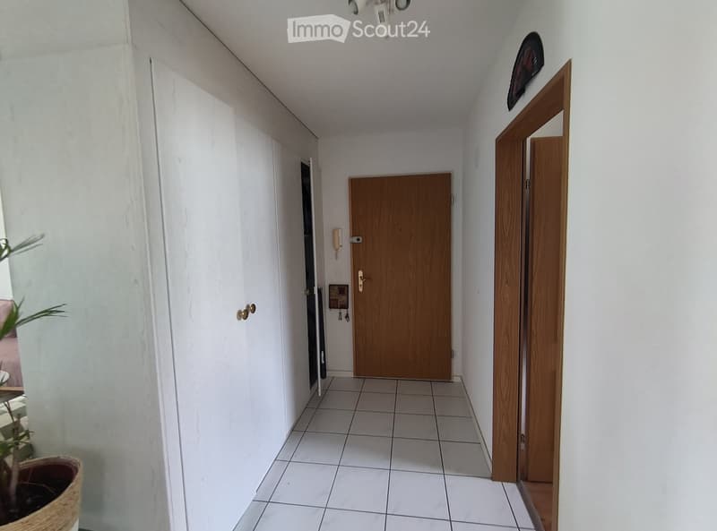 A clean, tiled hallway with white walls, wooden doors, and a small plant in a pot on the left side.