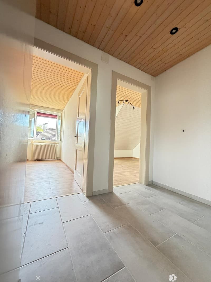 Bright hallway with tiled floor, white walls, wooden ceiling, and two open doors leading to other rooms.