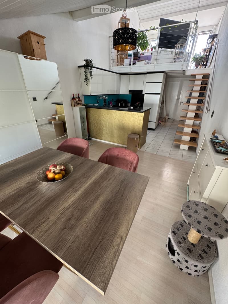 Open-plan living and dining area with a wooden dining table, pink chairs, a cat tree, a modern kitchen with white cabinets and a gold backsplash, and a staircase leading to an upper level.
