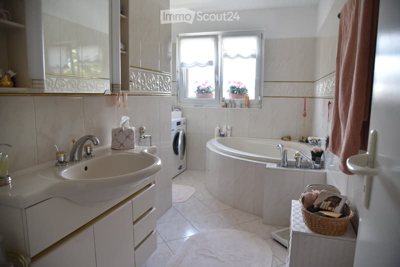 Bathroom with a double sink, bathtub, mirror, washing machine, and a small basket on a shelf.