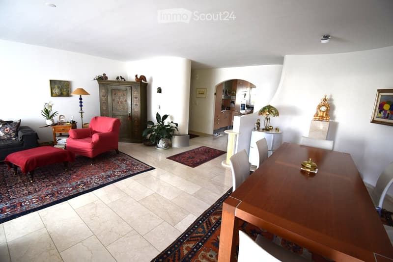 A well-furnished living and dining area with a sofa, red armchair, wooden dining table, and various decorative items including lamps, plants, and a cat tree.
