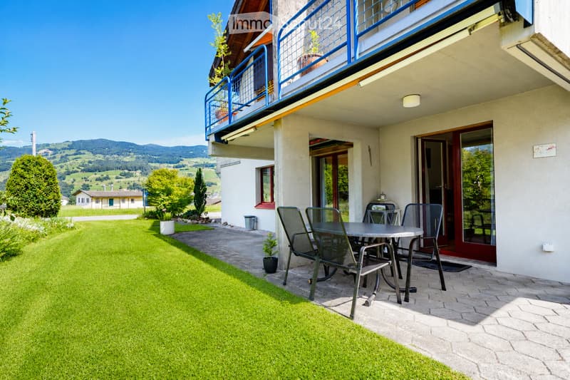 Garden area with a well-maintained lawn, a patio with a table and chairs, and a scenic mountain view in the background.