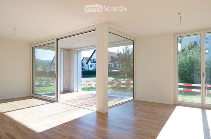 Empty room with wooden flooring and large glass sliding doors leading to an outdoor area. The space is bright and uncluttered, with no furniture or personal items visible.