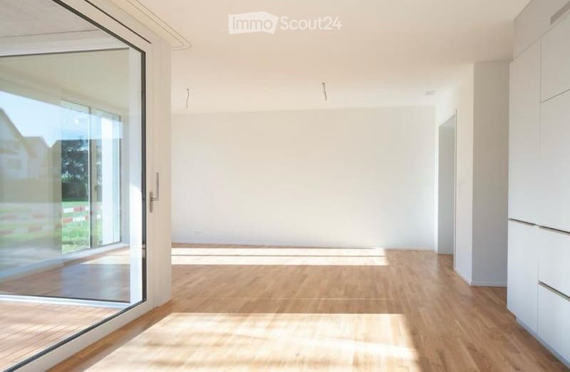 Empty room with wooden flooring, white walls, and large glass sliding door leading to outdoor area.
