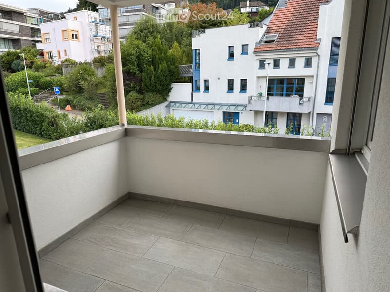 Balcony with tiled floor and white walls, overlooking a residential area with modern buildings and greenery.