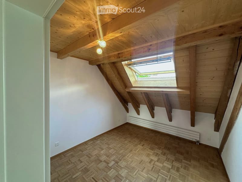 An empty attic space with wooden beams, exposed ceiling, skylight window, and wooden flooring.